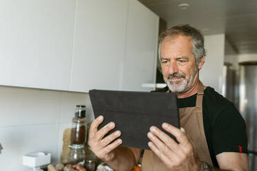 Mann benutzt digitales Tablet, während er zu Hause in der Küche steht - VABF03663