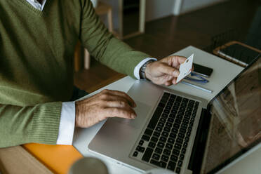 Midsection of mature man working on laptop while sitting at home - VABF03668