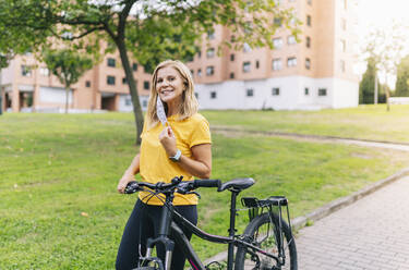 Lächelnde Frau mit Fahrrad auf dem Fußweg in der Stadt während COVID-19 - DGOF01569