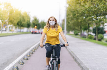 Woman wearing protective face mask cycling on bicycle lane in city - DGOF01570