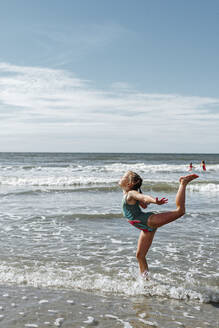 Girl doing gymnastics while standing in water at beach on sunny day - OGF00596