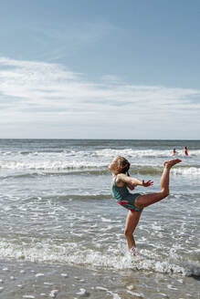 Mädchen beim Turnen im Wasser stehend am Strand an einem sonnigen Tag - OGF00596