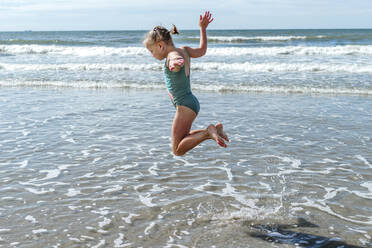 Girl gymnast jumping over sea at beach on sunny day - OGF00597