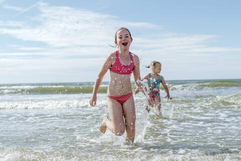 Girls running in water at beach on sunny day stock photo