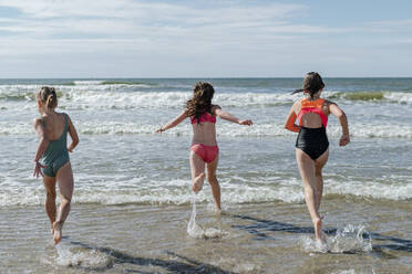 Friends running in water at beach on sunny day - OGF00599