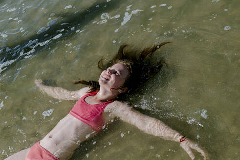 Mädchen liegt im Wasser am Strand an einem sonnigen Tag - OGF00600