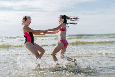 Freunde halten sich an den Händen, während sie an einem sonnigen Tag im Wasser spielen - OGF00604