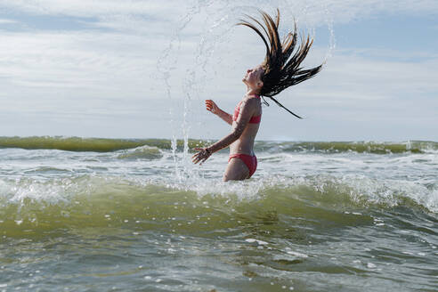 Mädchen mit zerzaustem Haar steht im Wasser am Strand an einem sonnigen Tag - OGF00605