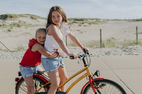 Younger sister embracing girl while sitting on bicycle during sunny day - OGF00609
