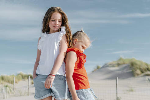 Sisters looking down while standing on beach during sunny day - OGF00610