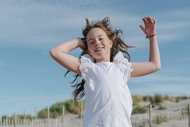 Mädchen mit Hand im Haar am Strand stehend an einem sonnigen Tag - OGF00611