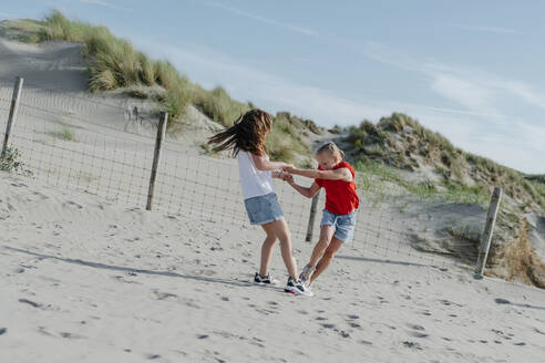 Sisters playing on sand at beach during sunny day - OGF00612