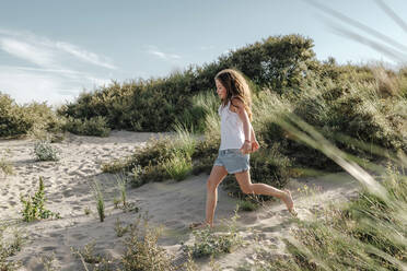 Mädchen läuft auf Sand am Strand während eines sonnigen Tages - OGF00613