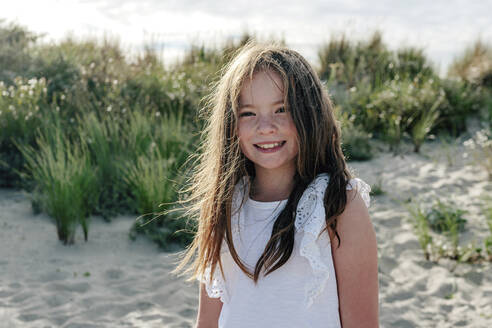 Lächelndes Mädchen, das an einem sonnigen Tag auf Sand am Strand steht - OGF00614