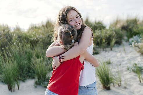 Sisters embracing each other at beach on sunny day - OGF00615