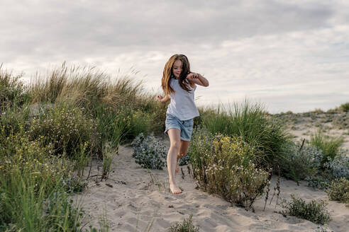 Cheerful girl running on sand at beach against cloudy sky - OGF00617