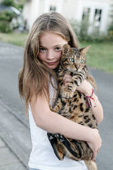 Girl carrying domestic cat while standing on street - OGF00621