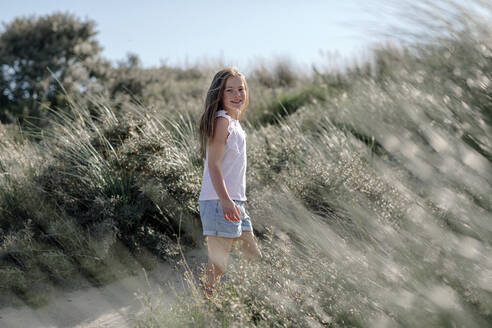 Girl standing in between of bush on sunny day - OGF00626