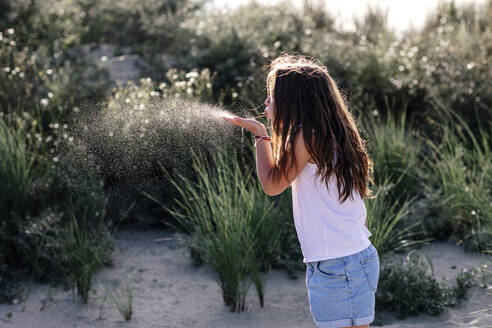 Girl blowing while standing on sand during sunny day - OGF00627