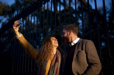 Lächelndes Paar, das ein Selfie mit dem Mobiltelefon macht, während es in der Stadt steht - OCMF01803