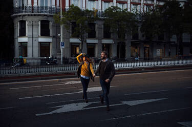 Husband and wife holding hand while crossing road in city - OCMF01805