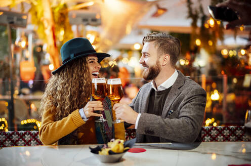 Paar stößt auf Bier an, während es im Biergarten in der Stadt sitzt - OCMF01815