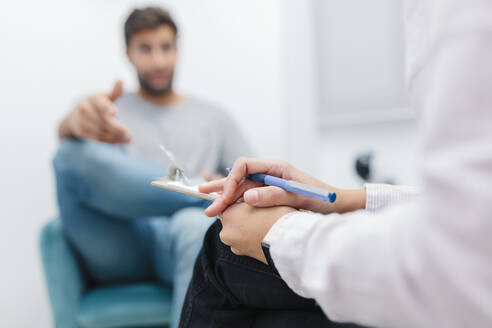 Doctor sitting with note pad while listening patient problems at office - MRRF00631