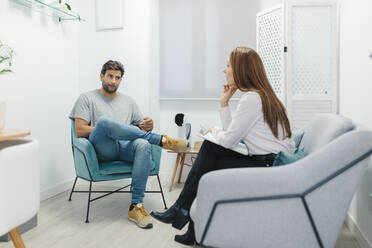 Psychologe hört sich das Problem eines Patienten an, während er auf dem Sofa im Büro sitzt - MRRF00633