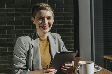 Frau benutzt digitales Tablet, während sie an einem sonnigen Tag in einem Café sitzt - MFF06701