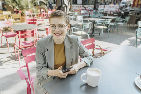 Woman looking away while using smart phone sitting in outdoor cafe stock photo