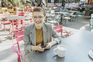 Frau schaut weg, während sie in einem Café im Freien sitzt und ihr Smartphone benutzt - MFF06706