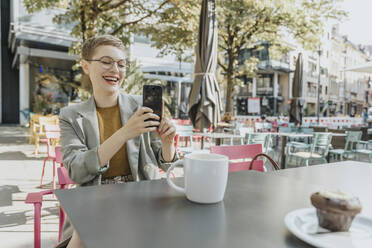 Frau, die ein Selfie mit ihrem Smartphone macht, während sie in einem Café im Freien sitzt - MFF06707