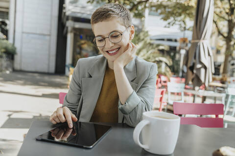 Woman using digital tablet sitting with hand on chin in sidewalk cafe stock photo