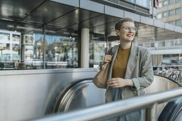 Lächelnde Frau, die auf einer Rolltreppe in der Stadt steht und wegschaut - MFF06716