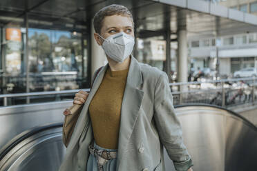 Frau mit Gesichtsschutzmaske, die beim Klettern auf einer Rolltreppe in der Stadt wegschaut - MFF06717