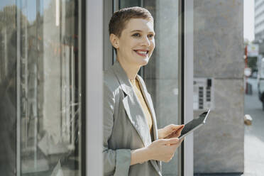 Mid adult woman using digital tablet while standing on street in city - MFF06720