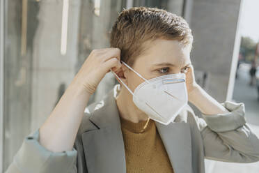 Mid adult woman wearing protective face mask standing on street during sunny day - MFF06725