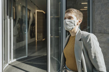 Mid adult woman wearing protective face mask standing in front of entrance - MFF06726