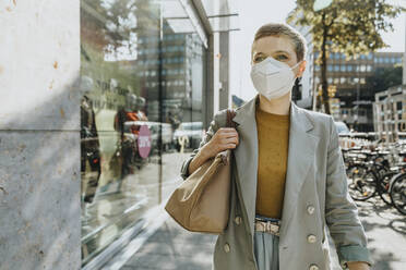 Woman wearing protective face mask walking on street during sunny day - MFF06729