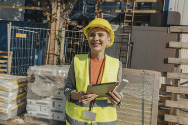 Lächelnde Frau, die auf einer Baustelle steht und ein digitales Tablet benutzt - MFF06732