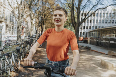 Frau mit elektrischem Tretroller auf der Straße an einem sonnigen Tag - MFF06733