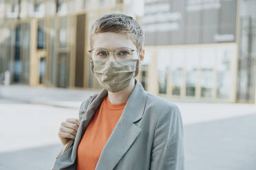 Woman wearing protective face mask standing on street in city during sunny day - MFF06744