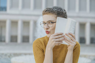 Mid adult woman hiding face with book while sitting on sunny day - MFF06766