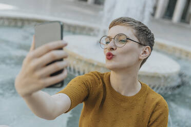 Mid adult woman taking selfie on smart phone standing against fountain - MFF06771