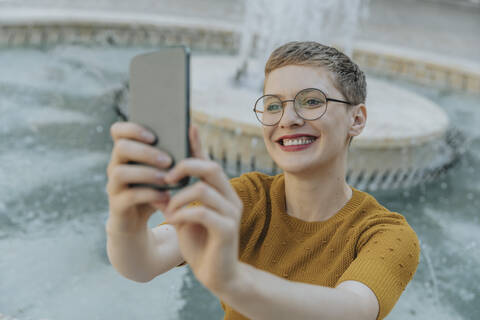 Smiling mid adult woman taking selfie on smart phone standing against fountain stock photo