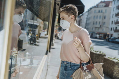 Woman wearing protective face mask doing window shopping while standing on street in city stock photo