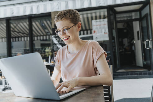 Woman using laptop sitting in sidewalk cafe on sunny day - MFF06785