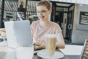 Lächelnde Frau mit Laptop in einem Straßencafé an einem sonnigen Tag - MFF06787