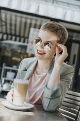 Mittlere erwachsene Frau mit Sonnenbrille und Kaffeeglas in einem Straßencafé an einem sonnigen Tag - MFF06797