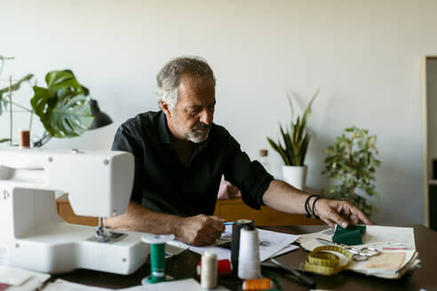Älterer männlicher Kostümbildner, der bei der Arbeit im Atelier den Stoff überprüft - VABF03686